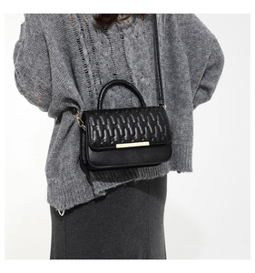 Detalle de bolso acolchado negro con herrajes dorados y textura de pliegues verticales