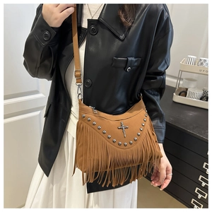 Detail of brown suede crossbody bag with silver studs and tassel fringe on a leather jacket