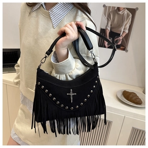 Detail of vintage black suede shoulder bag with rivets, fringe, and a cross pendant