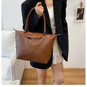 Detail of brown faux leather tote bag with metallic snap button and reinforced stitching