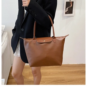 Detail of a brown leather tote bag with a zipper closure and a semicircular flap buckle