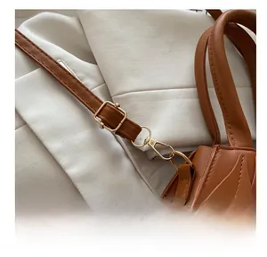 Detail of adjustable golden buckle and lobster clasp on a caramel leather shoulder bag