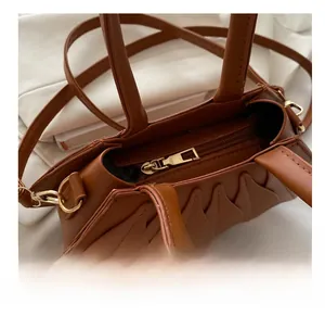 Detail view of brown leather handbag with smooth gold zipper and wave pleated side