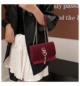 Detail of burgundy velvet crossbody bag with V-shaped quilting and gold tassel charm