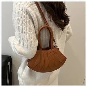 Brown fan-shaped leather handbag with unique leaf-layered design worn over a white sweater