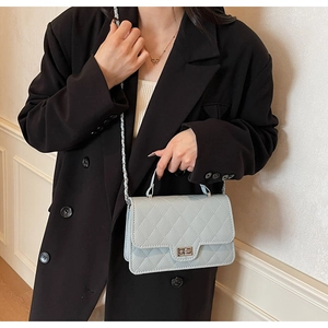 Detail of grey quilted handbag with chain strap and metal handle on a black blazer