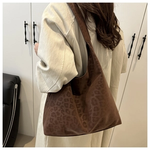 Detail of a large leopard print hobo bag in dark brown faux suede shown on a shoulder