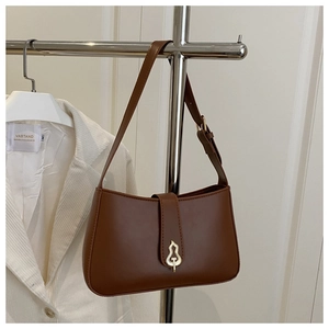Detail of dark brown leather underarm bag with unique gold artistic metal buckle closure