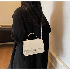 Detail of white quilted crossbody bag with metal chain strap and turn-lock closure