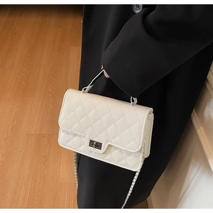 Detail of white quilted crossbody bag featuring metal turn-lock and leather texture