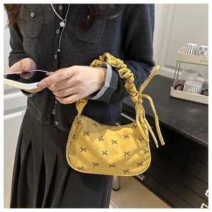 Street style shot of yellow corduroy handbag with black bows and pleated handle