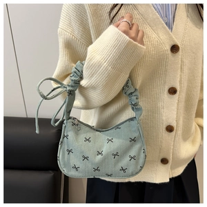 Detail of light blue corduroy shoulder bag with black bow prints and ruffled handle