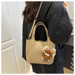 Close-up of beige lychee pattern bucket bag with a cute brown monster plush charm