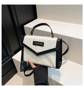 Close-up of woven leather texture and black V-shaped trim on a minimalist handbag