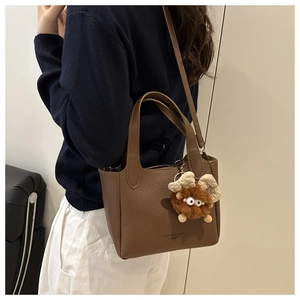 Detail of dark brown lychee leather bucket bag with plush monster charm on model