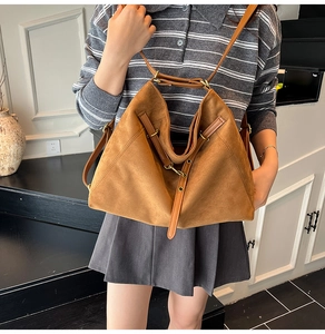 Détail d'un grand sac hobo en daim marron avec doubles bretelles en cuir et anneaux métalliques