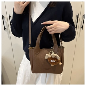 Detail of brown litchi leather bucket bag with plush charm on a fashion model
