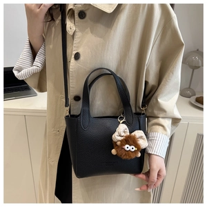 Détail du sac seau en cuir noir grainé avec un pendentif en peluche marron doux