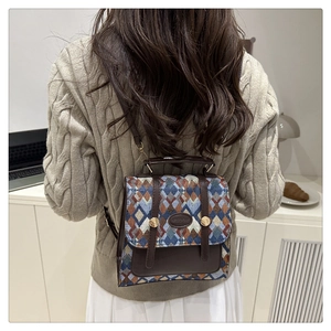 Detail view of a retro woven plaid backpack with brown leather flap on a beige sweater