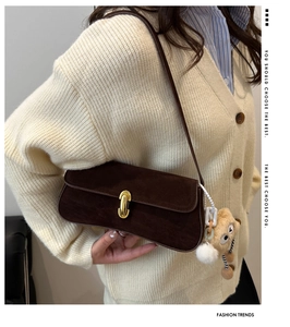 Détail d'un sac baguette en daim marron avec boucle dorée et breloque en forme d'ours