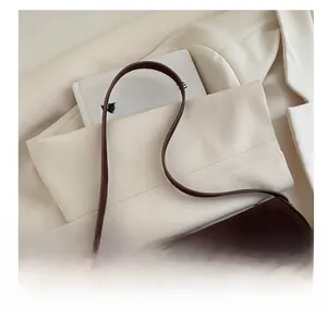 Détail du sac à bandoulière en daim marron foncé avec boucle dorée sur blazer beige