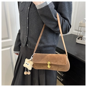 Detail of brown suede shoulder bag with golden twist lock and plush charm on model