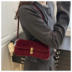 Close-up of burgundy suede shoulder bag featuring a gold metal lock and bear charm