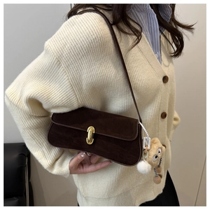 Detail of dark brown suede shoulder bag with a gold twist lock and a cute plush bear charm