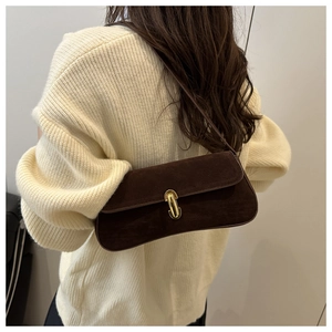 Detail of a dark brown suede baguette bag with a gold lock worn on the shoulder