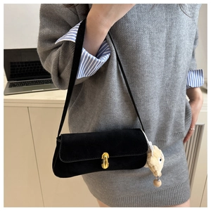 Detail of black suede underarm bag with gold metal clasp and a plush charm accessory