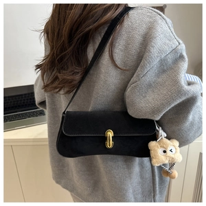 Detail of black suede baguette bag with gold buckle and plush charm on a model