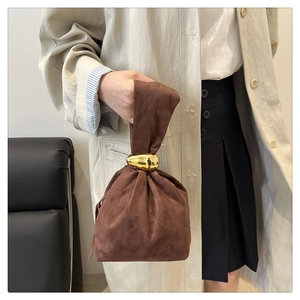 Détail d'un sac seau en daim avec poignée métallique dorée unique et texture marron doux
