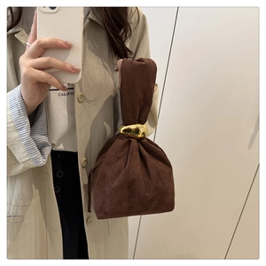 Détail du sac seau en daim marron foncé avec une grande poignée en anneau doré poli