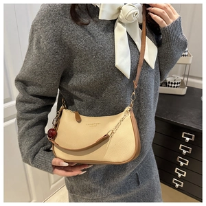 Detail of beige hobo bag with cherry charm, leather strap and gold chain accessories