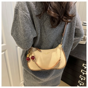 Close-up of beige lychee leather bag featuring red cherry charm and golden hardware detail
