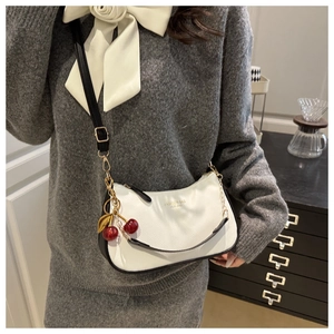 Close-up of a white lychee leather crescent bag with a cute red cherry bag charm