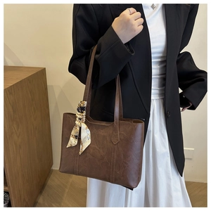 Detail einer braunen Shopper-Tasche mit gemustertem Seidenschal am Schulterriemen