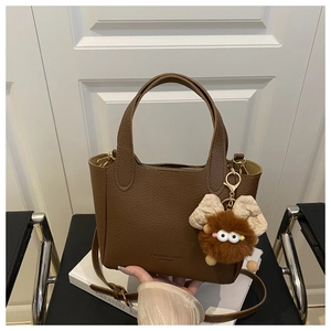 Détail du sac seau en cuir marron à motif litchi avec un pendentif peluche mignon