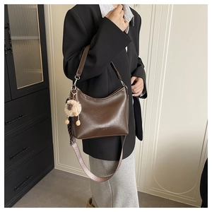 Détail du sac seau en cuir marron avec bandoulière tissée et breloque peluche sur fond vintage
