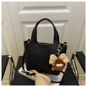 Détail du sac seau noir en cuir grainé avec breloque monstre poilu sur un livre blanc