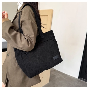 Detail of black corduroy tote bag showing ribbed texture and shoulder straps on model