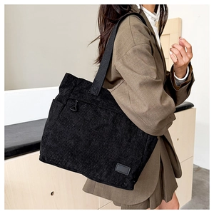 Detail of black corduroy tote bag showing ribbed texture and metal zipper hardware