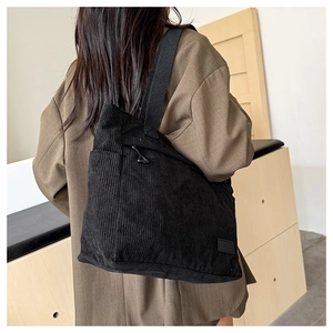 Close-up of black corduroy tote bag showing vertical stripe texture and wide shoulder strap