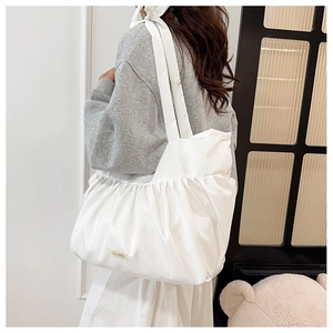 Detail of white pleated tote bag with bow shoulder strap and golden metal logo tag