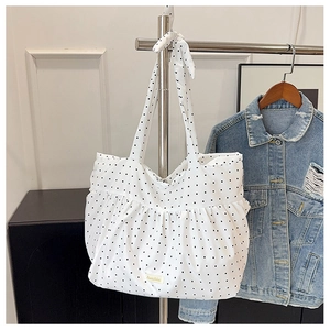 Detailed view of white polka dot tote bag with pleated ruffle design on a metal hanger