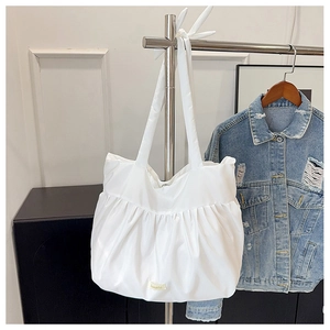 Detail view of white pleated tote bag with long handles and a minimalist woven brand label