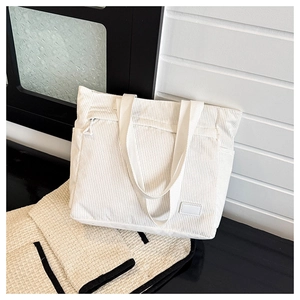 Detailed texture of white corduroy tote bag showing front zipper pocket and shoulder strap