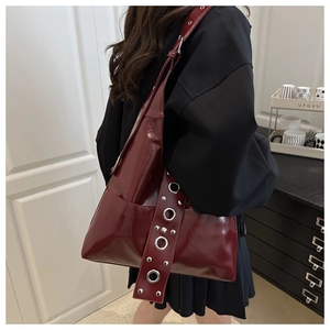 Detail of burgundy glossy tote bag with large silver eyelets on the shoulder strap