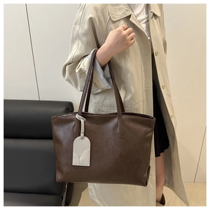 Detail of a large brown leather tote bag with grey tag charm worn on the shoulder