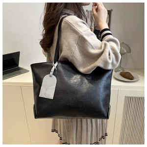 Close-up of the pebbled leather texture and minimalist pendant on a black tote bag